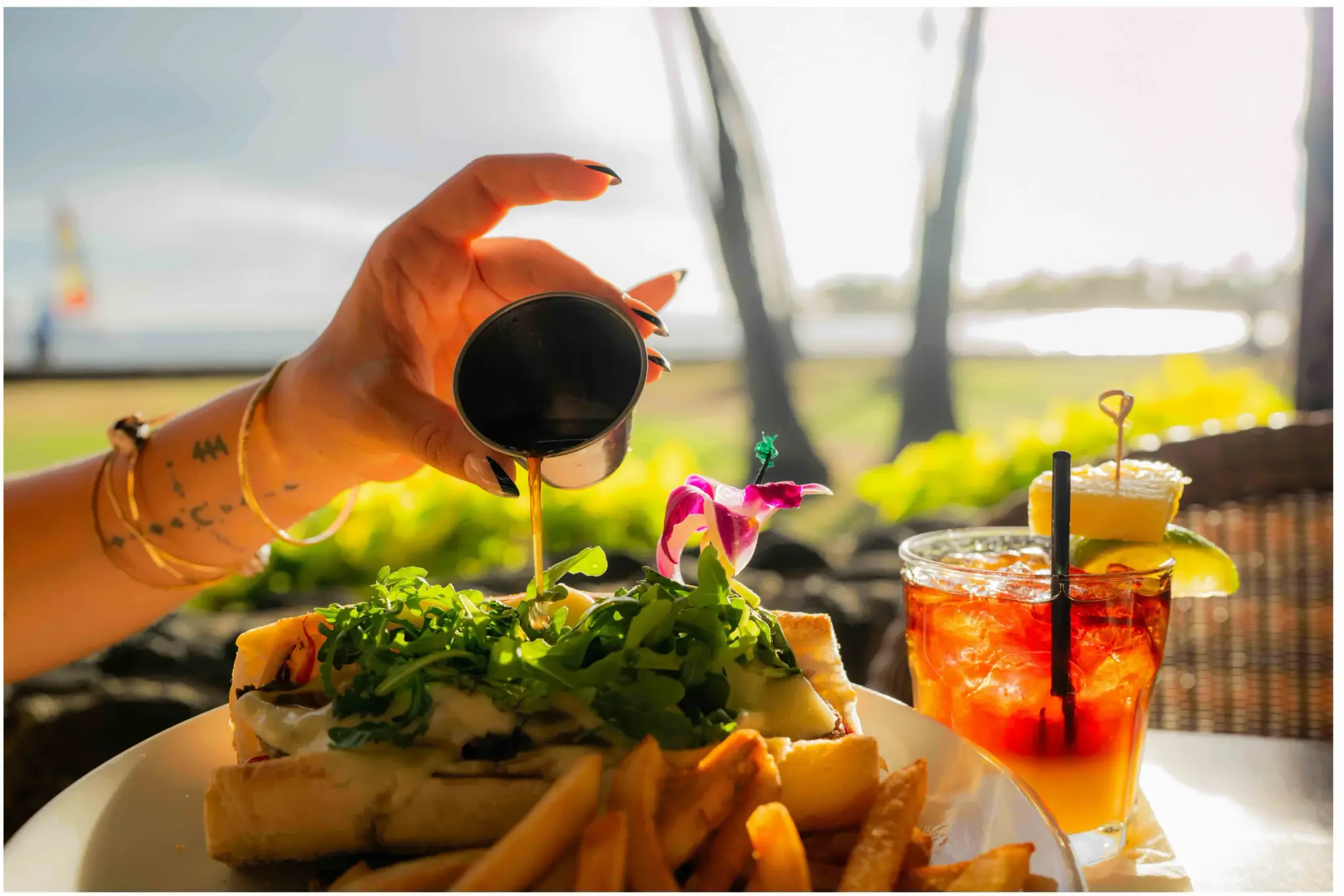 Au jus poured over the Prime Rib Sandwich at Kona Inn Restaurant, with French fries and cocktails on the oceanfront lanai