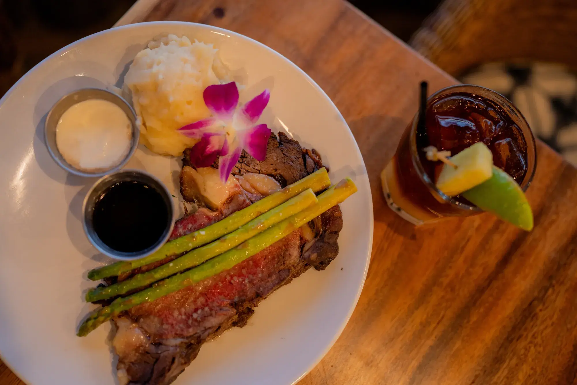 Kona Cut Prime Rib at Kona Inn Restaurant with grilled asparagus, garlic mashed potatoes, au jus and horseradish cream, beside a cocktail