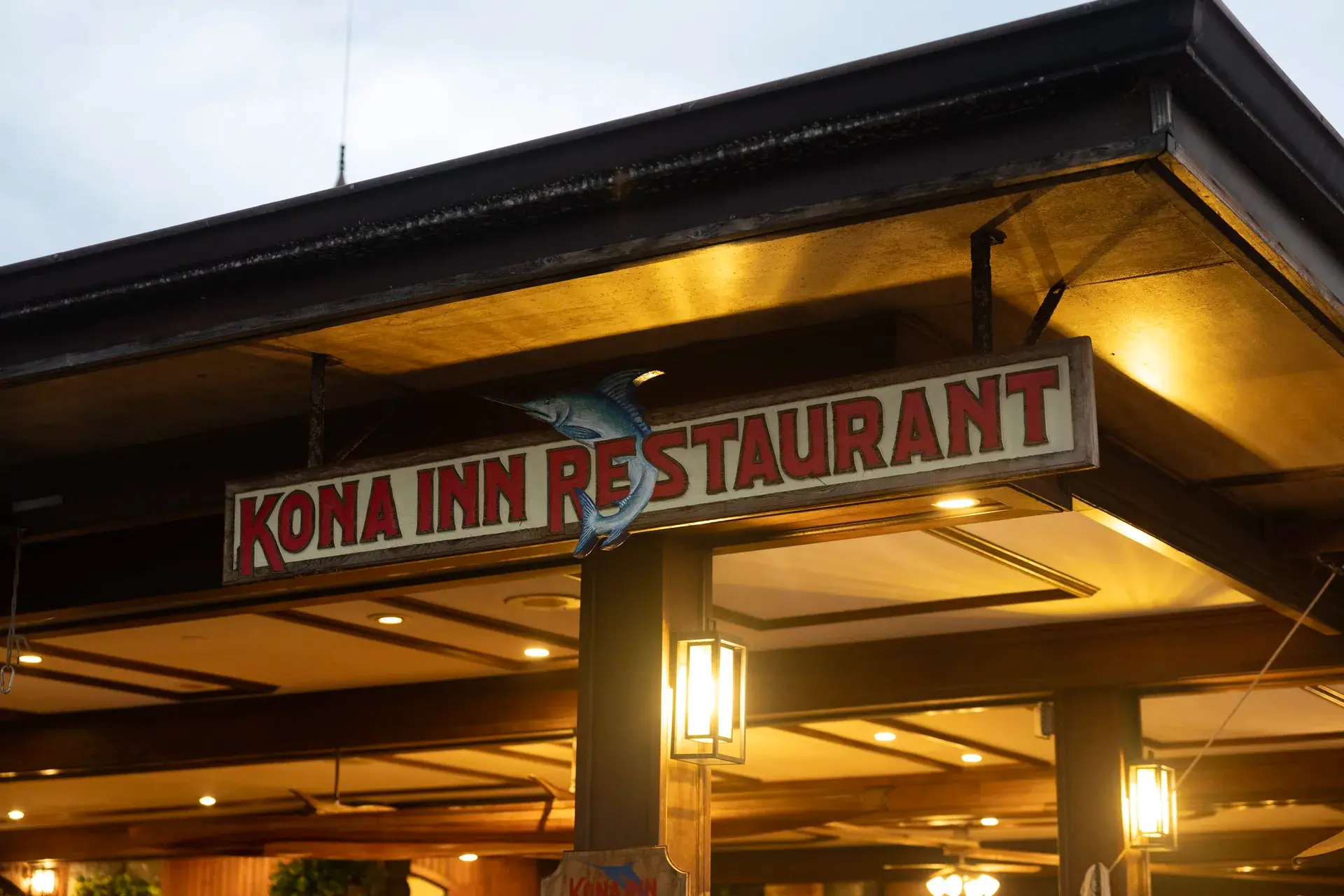 The lit Kona Inn Restaurant entrance sign at dusk on Aliʻi Drive in historic Kailua-Kona