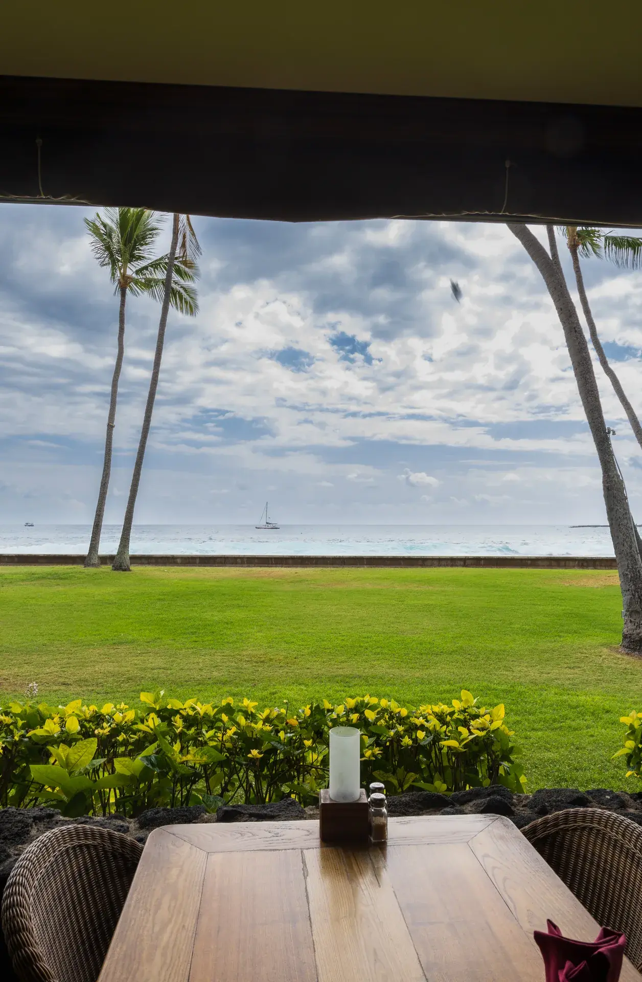 Kona Inn Restaurant lawn opening onto Kailua Bay with palm trees, the Pacific, and sailboats on the water