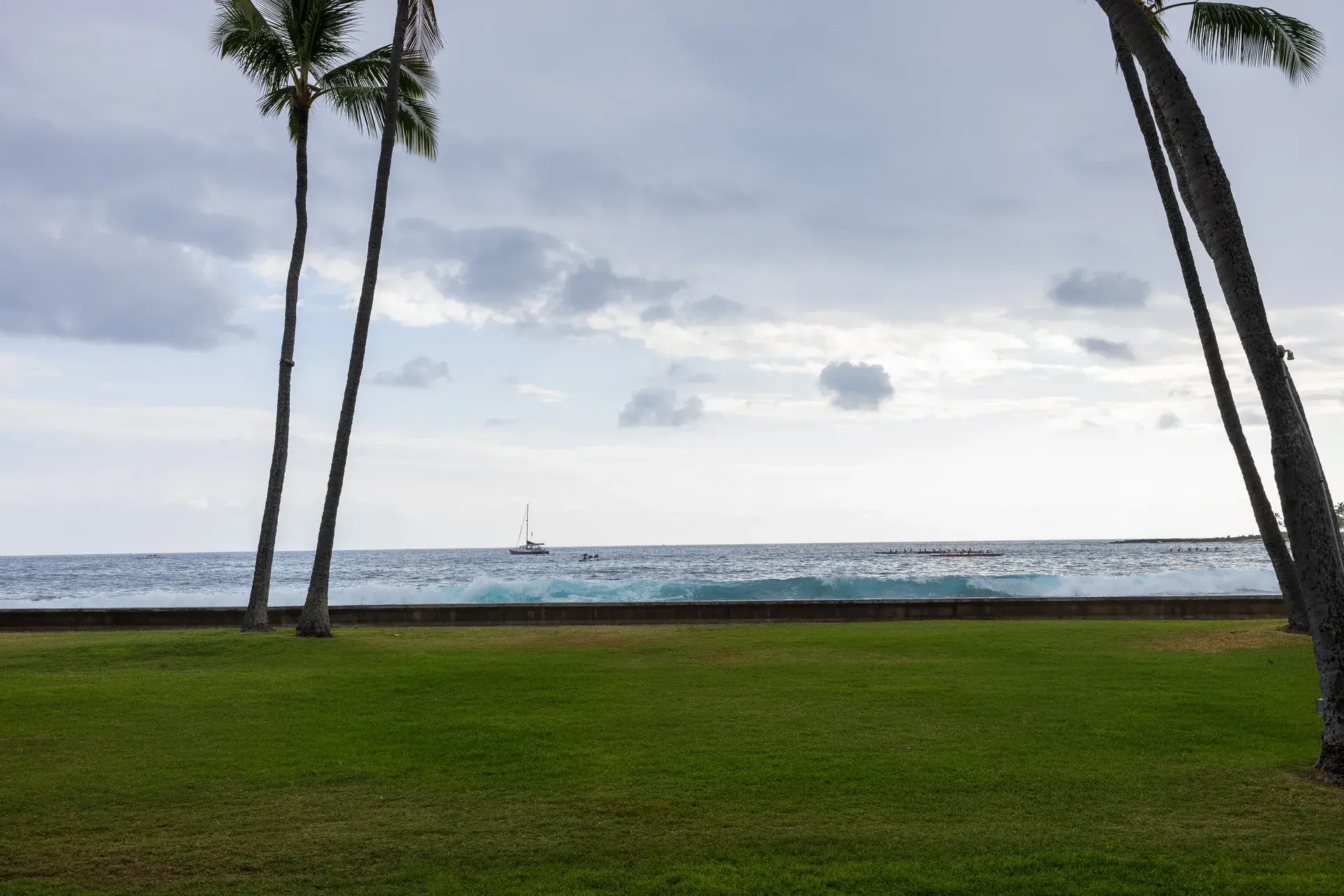 Pacific Ocean view with palms and a sailboat off Aliʻi Drive at Kona Inn Restaurant in Kailua-Kona