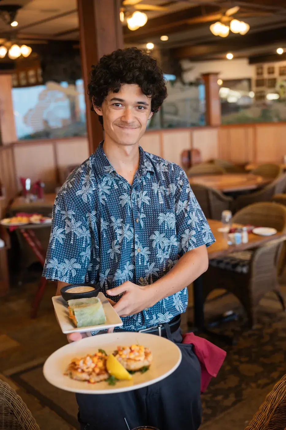 Kona Inn server in an aloha shirt bringing a plate to the table in the oceanfront dining room